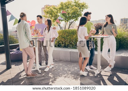 Full body portrait of beautiful fellows stand around table hands hold champagne talk listen meeting restaurant outdoors