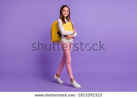 Full length body size photo of female pupil walking embracing book carrying yellow bag smiling isolated on vivid violet background Royalty-Free Stock Photo #1851092323
