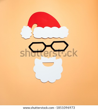 paper, red Santa Claus hat with a white beard on a beige background, top view