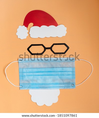paper, red Santa Claus hat with white beard and medical mask on beige background, top view