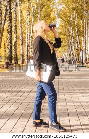 Young woman drink coffee and hold laptop in park, full lenght. Remote work concept.