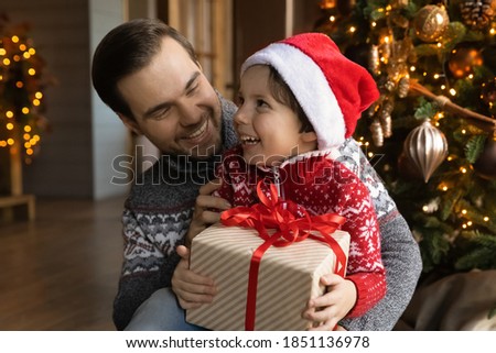 Overjoyed loving young Caucasian father and small son celebrate New Year at home together. Caring dad greeting congratulating excited little boy child present Christmas gift. Winter holiday concept.