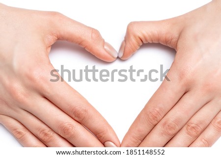 Closeup of hands of young woman forming shape of heart with her manicured fingers on white background