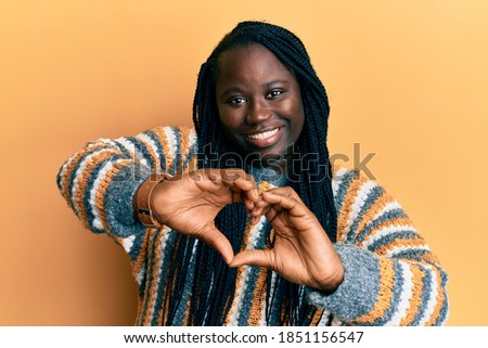 Young black woman with braids wearing casual winter sweater smiling in love doing heart symbol shape with hands. romantic concept. 