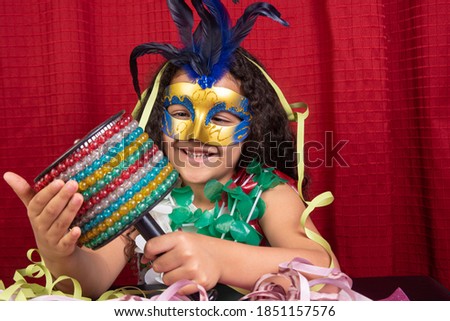 Little girl with mask and streamers and carnival instruments from Brazil, red background, selective focus.