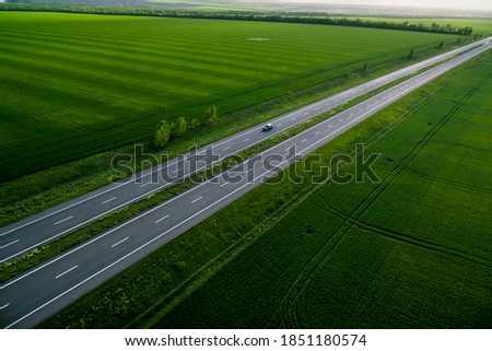 black car driving on asphalt road along the green fields. seen from the air. Aerial view landscape. drone photography.  travel concept. Sunset time
