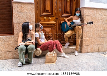 Young girl playing guitar to her friends with masks on in the middle of the street