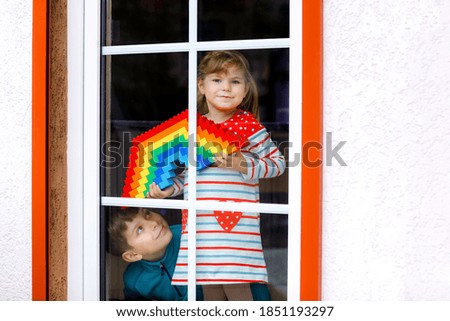 Toddler girl and kid boy by window create rainbow with colorful plastic blocks during pandemic coronavirus quarantine. Two children, siblings made and paint rainbows around the world as sign.