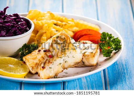 Fish dish - fried cod fillet with curly french fries and vegetable salad on wooden table
