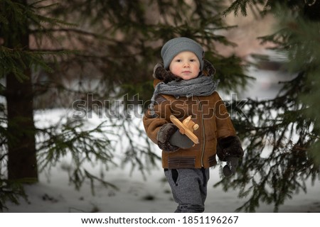 Little boy walks in the winter park. The boy stands near the Christmas tree. The boy has a wooden toy in his hand. Image with selective focus.