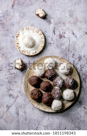Raw vegan homemade coconut chocolate candy balls with coconut flakes in ceramic plate over white wooden background. Flat lay, copy space