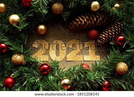 Gold, glittering numbers 2021 in frame of Christmas tree with cones and decorations on wooden background. New Year greeting horizontal banner