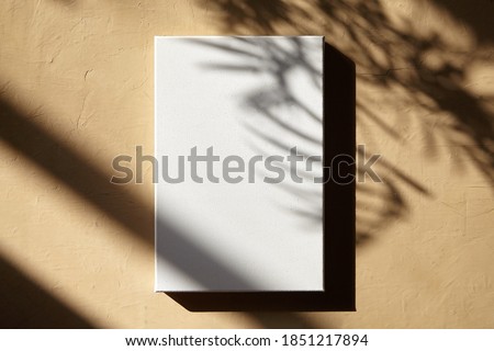 White canvas hanging on wall with shadows of leaves. Poster mockup, blank cotton canvas