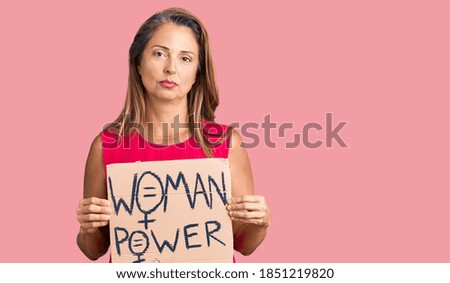 Middle age hispanic woman holding woman power banner thinking attitude and sober expression looking self confident 
