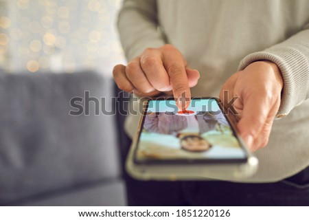 Find love online concept. Adult woman pressing red heart like button below handsome man's profile photo on dating app. Close-up of female hands holding mobile phone. Soft focus, selective focus, blur