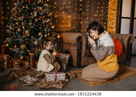 Mother taking pictures of her daughter at home, next to a christmas tree.