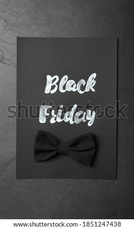 Card with phrase Black Friday and bow tie on dark background, top view