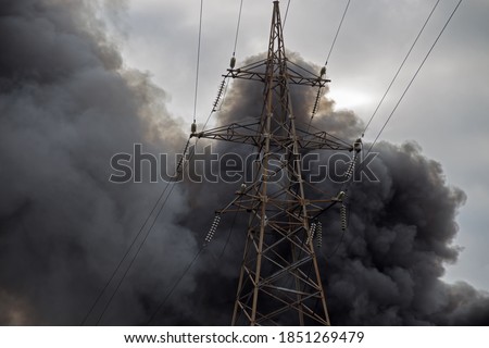 Black smoke from a fire over the city against a cloudy sky with a high-voltage tower Royalty-Free Stock Photo #1851269479
