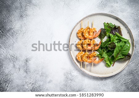 roasted shrimps, prawns on skewers with spinach salad. Gray background. Top view. Copy space