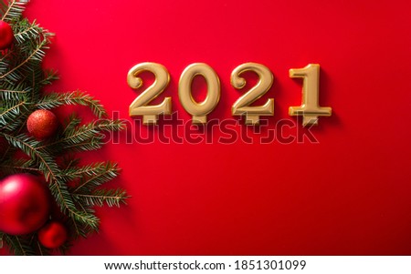 The numbers 2021 and a Christmas tree branch with red toy ballson red background, advertising photo.