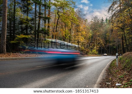 Car speeding on a countryside road during fall amongst trees in Europe