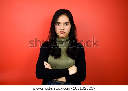 Portrait of Young beautiful asian women using black sweater folded arms and angry with red isolated background