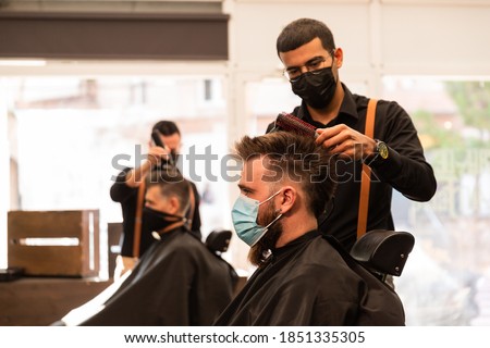 in a barber shop barbers cut the hair of two clients during the pandemic, they wear a coronavirus protective mask. they are caucasian and latin, multiethnic. Royalty-Free Stock Photo #1851335305