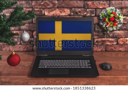 Christmas, new year's composition. Branches of the tree are decorated with Christmas balls on the background of a laptop with the image of the flag of Sweden
