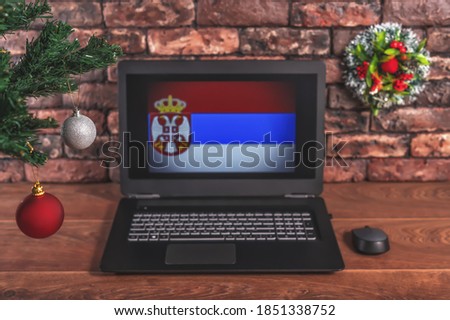 Christmas, new year's composition. Branches of the tree are decorated with Christmas balls on the background of a laptop with the image of the flag of Serbia