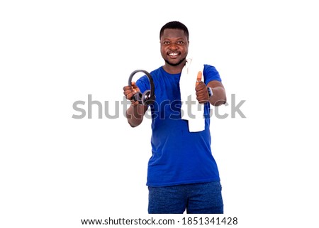 young man in sportswear standing against white background giving somebody headphones and making okay gesture smiling.