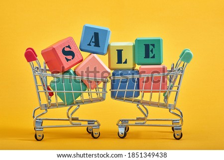 A miniature shopping cart and multi-colored cubes on yellow background. Sales word written on cubes.