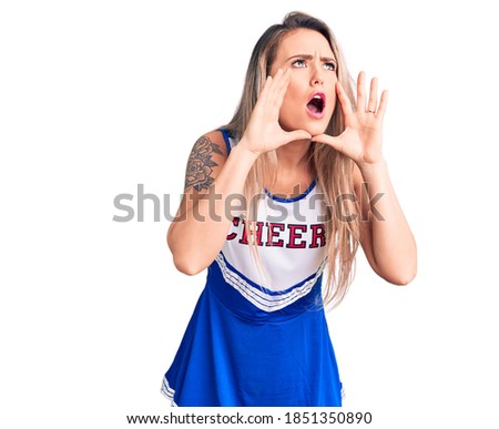 Young beautiful blonde woman wearing cheerleader uniform shouting angry out loud with hands over mouth 