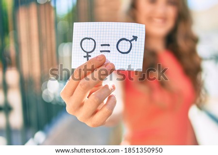 Young blonde girl smiling happy holding paper with gender equality concept walking at the city. Royalty-Free Stock Photo #1851350950