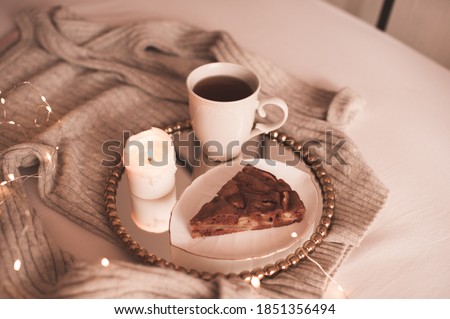 Chocolate pie with cup of tea and burning candle on tray with knitted sweater in bed close up. Good morning. Winter season. 