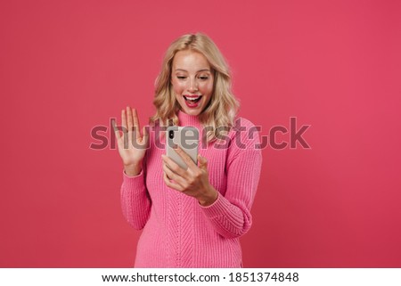 Pretty young blonde woman girl in sweater posing isolated on pink background, on a video call through mobile phone