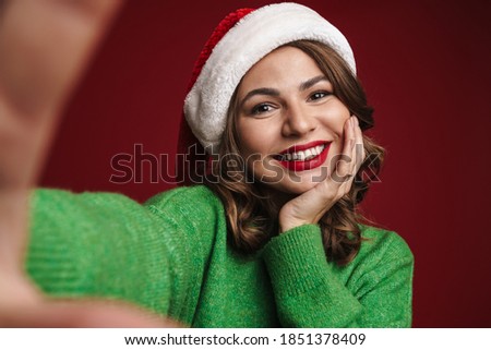 Happy girl in Santa Claus hat taking selfie photo isolated over red background