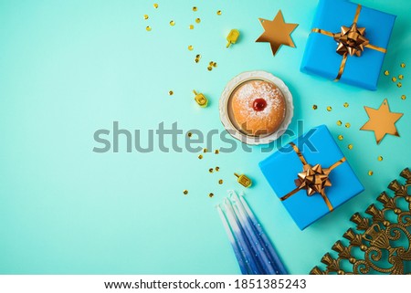 Jewish holiday Hanukkah concept with menorah, sufganiyah, gift box and spinning top over blue background