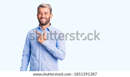 Young handsome blond man wearing elegant shirt cheerful with a smile on face pointing with hand and finger up to the side with happy and natural expression 