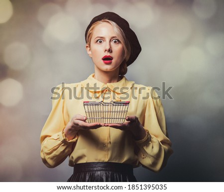 Beautiful girl in vintage clothes with shopping basket on gray background