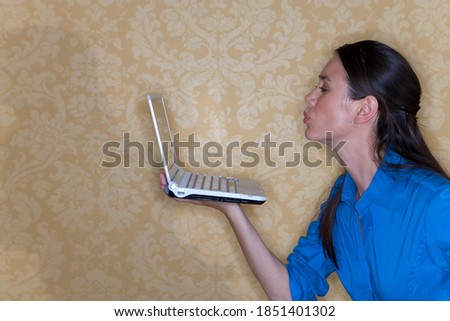 Close up of a young woman with straight black hair holding a laptop in her hand and blowing a kiss at the screen