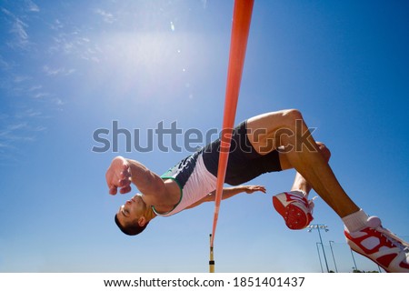 Young male pole vaulter jumping over a bar during a practice session at the track on a bright, sunny day with a clear blue sky in the background Royalty-Free Stock Photo #1851401437