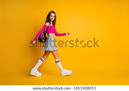 Full length profile photo of cute lady curly hairstyle step smile wear backpack pink top unclothed shoulders mini skirt stockings sneakers isolated yellow color background