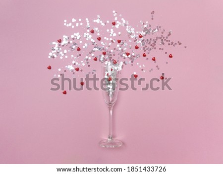 glass of champagne with glitter confetti and red hearts on the pink background with copy space. present gift card. Invitation of the party. christmass, valentines day and new year.
