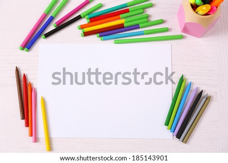 Colored pencils and blank paper sheet on wooden table
