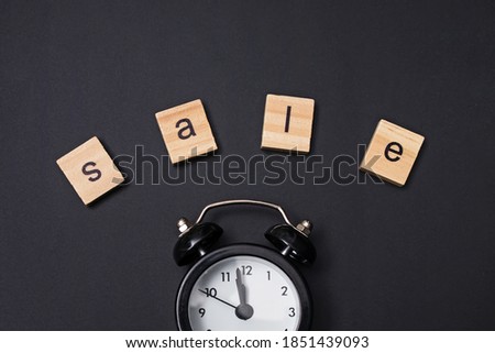 Small alarm clock and word Sale on black background, top view. Black friday concept