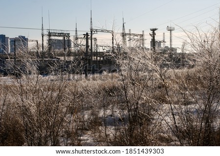Image of industrial and residential buildings against the background of picturesque branches on trees in the foreground in frost on a frosty Sunny day and blue sky in the background light.