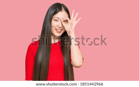 Young chinese woman wearing casual clothes doing ok gesture with hand smiling, eye looking through fingers with happy face. 