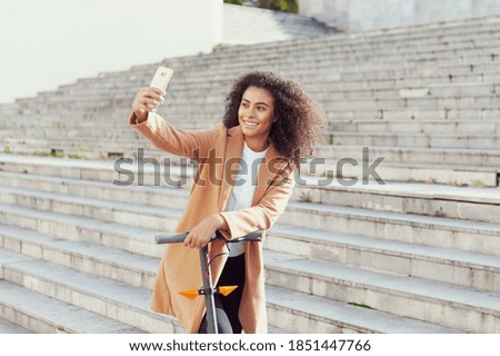 woman takes a selfie photo with the mobile phone has an electric scooter in the street