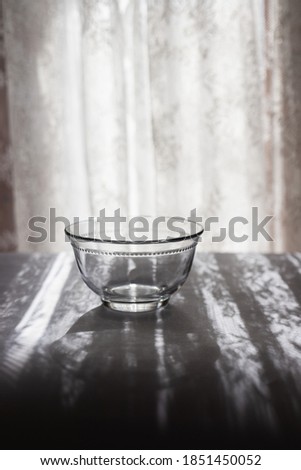 Empty glass bowl or cup in front of a sunny window with a lace curtains, and beautiful shadows on the table. Simple, minimalist vertical shot