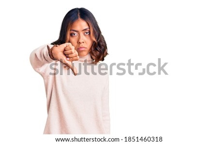 Young beautiful mixed race woman wearing winter turtleneck sweater looking unhappy and angry showing rejection and negative with thumbs down gesture. bad expression. 